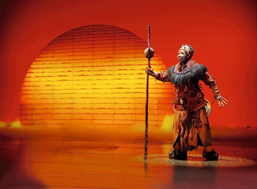 Die Schamanin Rafiki vor der aufgehenden Sonne im Musical DER KÖNIG DER LÖWEN